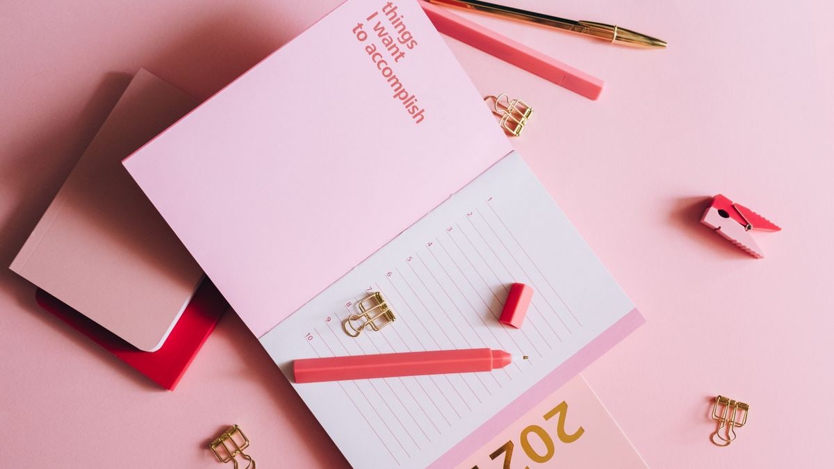 Organized workspace with pink planner, pen, and clips on pastel background.